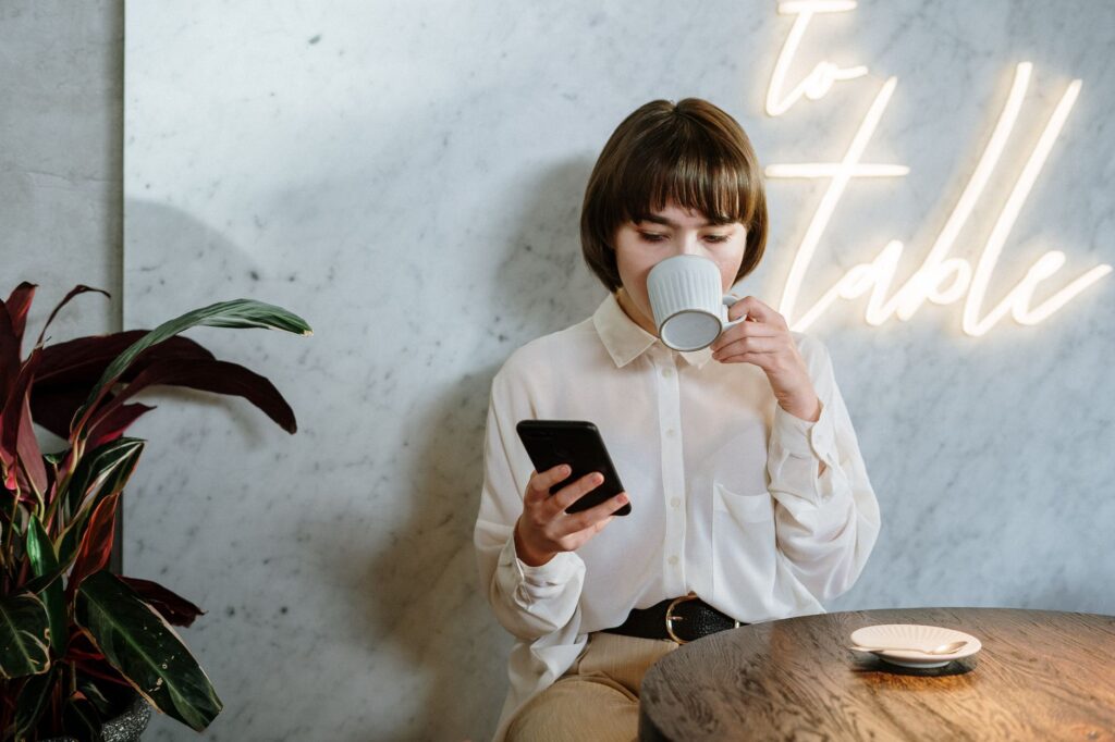 Młoda kobieta w kawiarni korzysta z telefonu przy kawie i neonowym świetle
