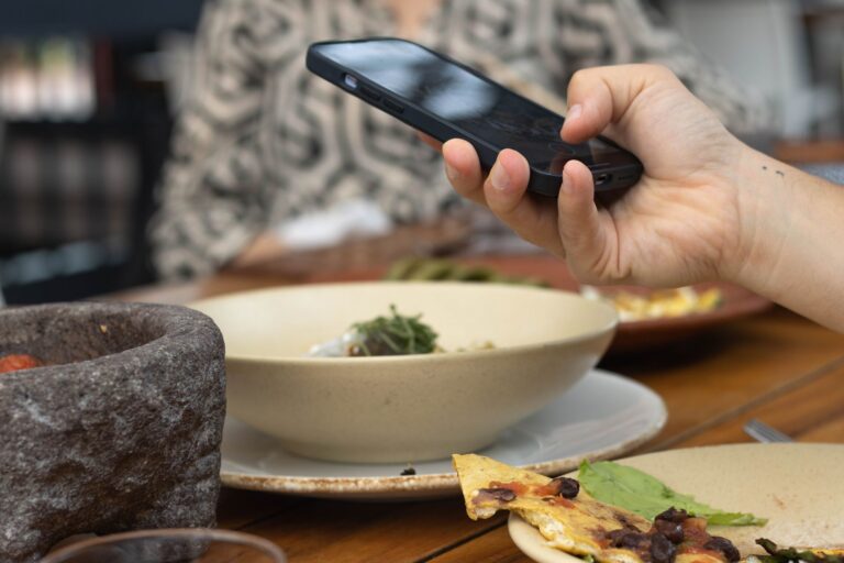 Osoba fotografuje posiłek smartfonem przy stoliku w restauracji